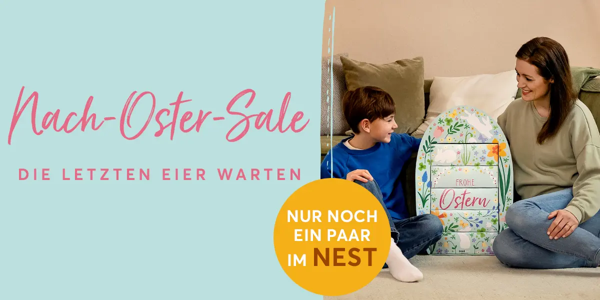 Mutter und Sohn sitzen in einem gemütlichen Wohnzimmer vor dem Sofa auf dem Boden. Zwischen ihnen steht das bunt dekorierte, riesiges brandnooz Osterei mit der Aufschrift "Frohe Ostern". Das Ei ist fast genauso groß wie der etwa 8 jährige Junge.